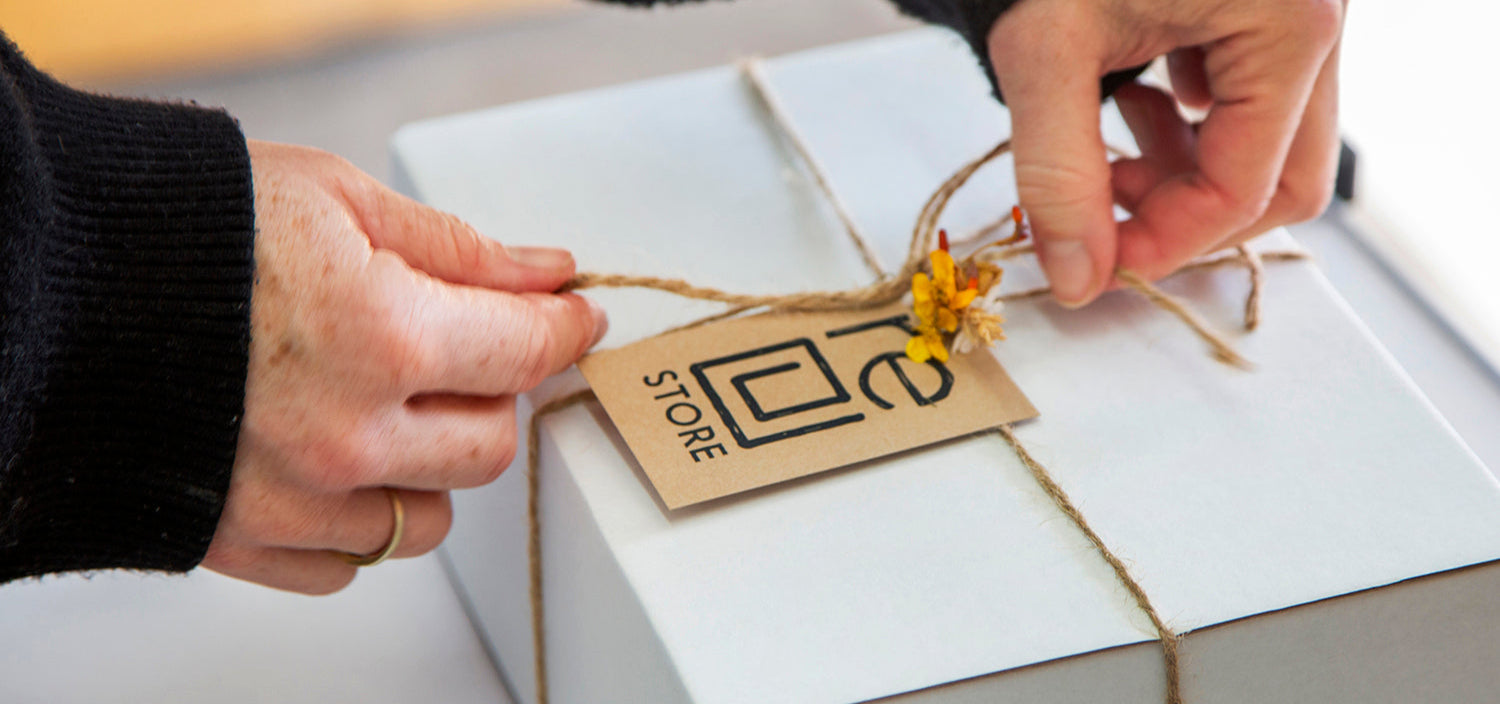 Person tying a decorative string on a nz made gift box with a tag
